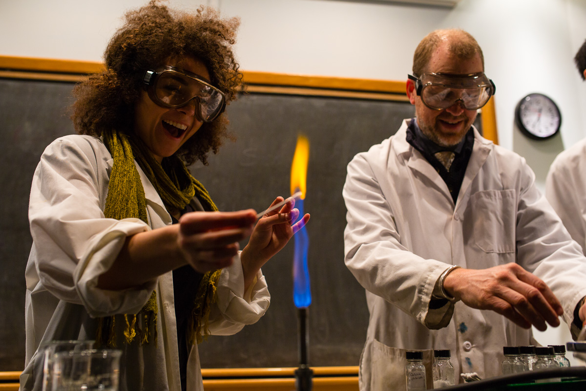 Student lighting Bunsen burner with teacher in background